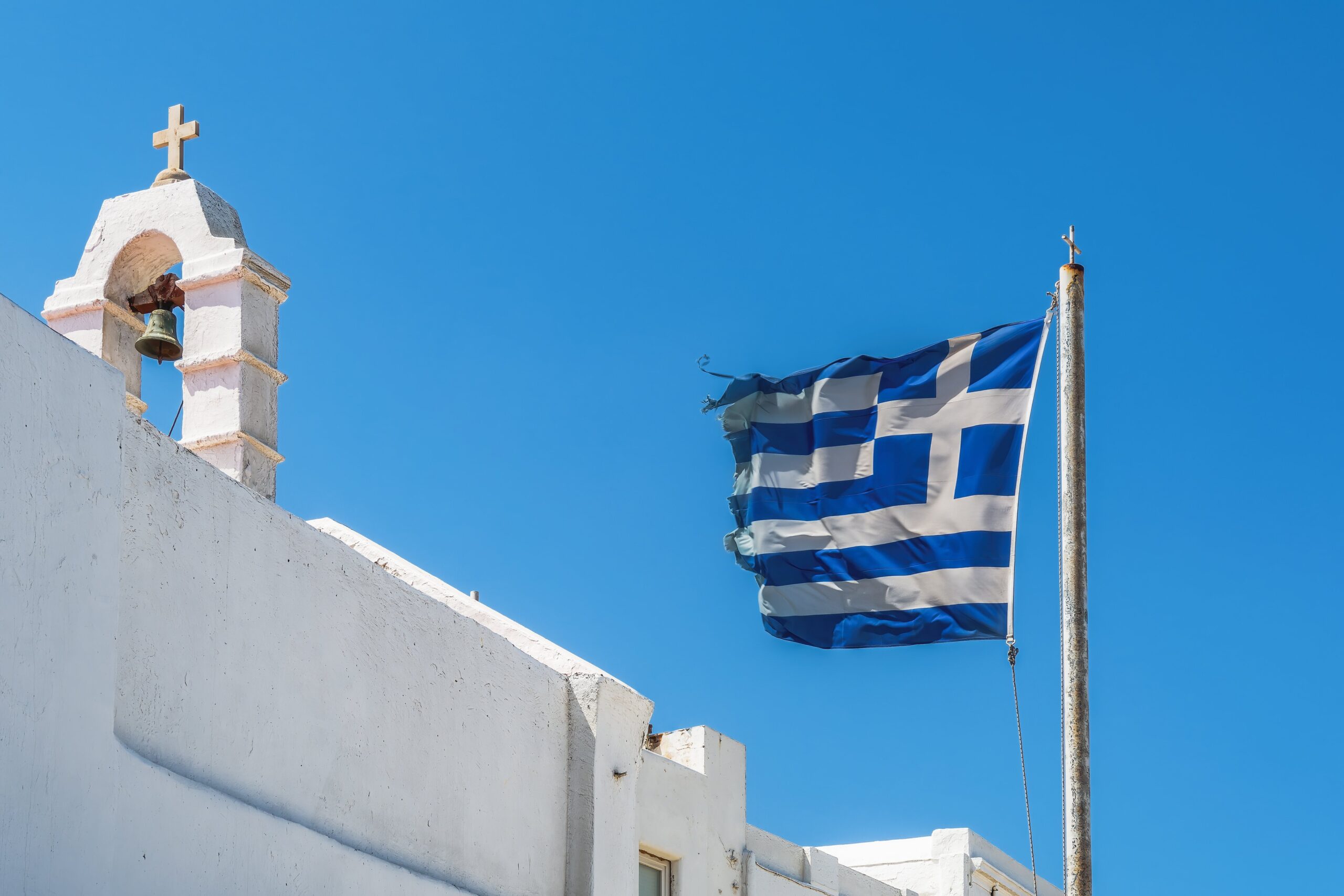 Cruz ortodoxa griega bandera griega ondeando antes de pintar la iglesia contra el cielo azul