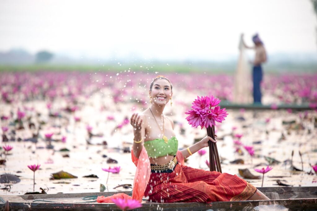 Mujer asiática tailandesa con pétalos de loto rosa en el aire sentada en un bote en el lago